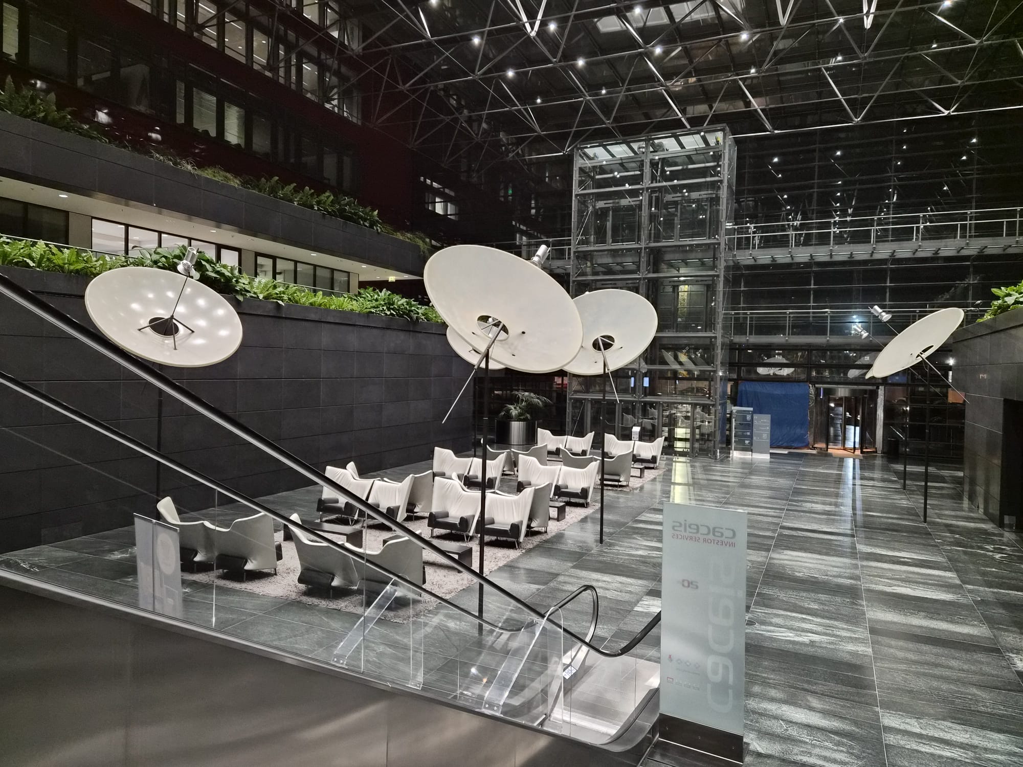 Intérieur moderne du bâtiment de l’Université Populaire Belval à Esch-sur-Alzette, avec un grand atrium vitré, des fauteuils blancs disposés en cercle pour la formation d’improvisation théâtrale, des lampes design suspendues et une atmosphère lumineuse et accueillante.